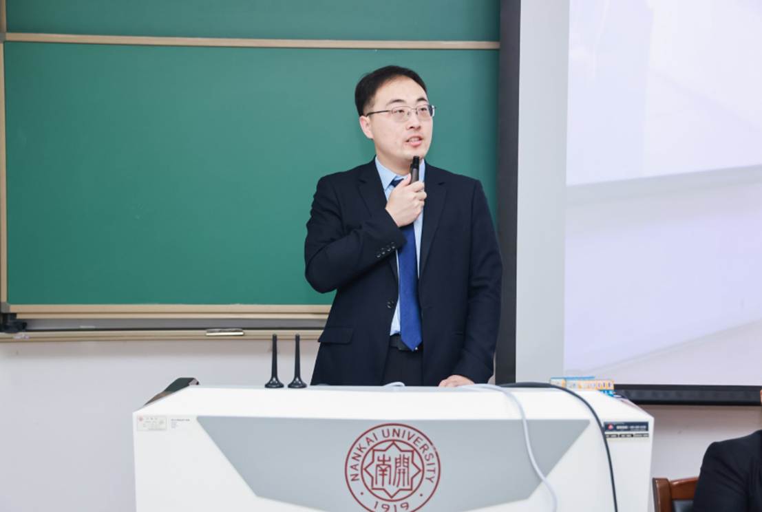 A person in a suit standing in front of a green board Description automatically generated